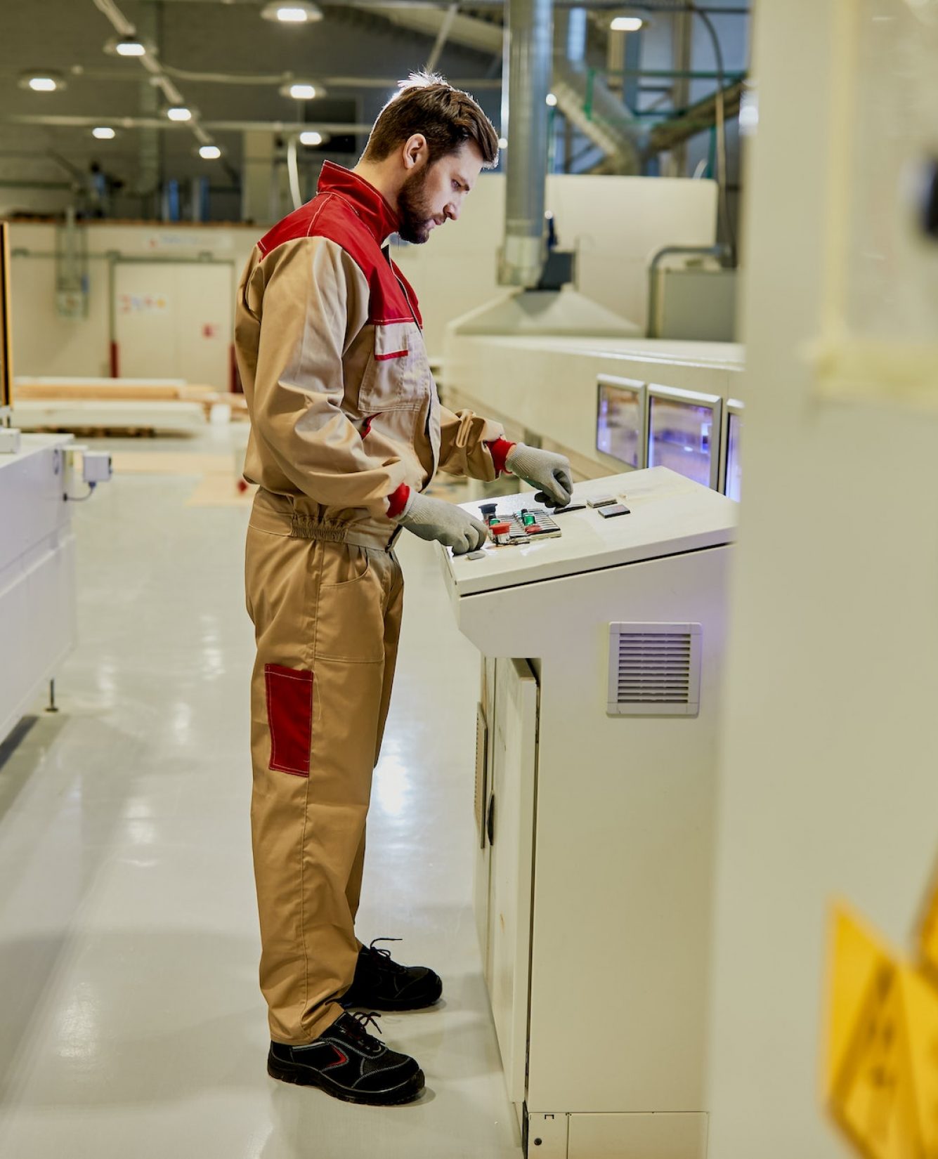 Full length of a worker operating woodworking machine at production line in a factory.